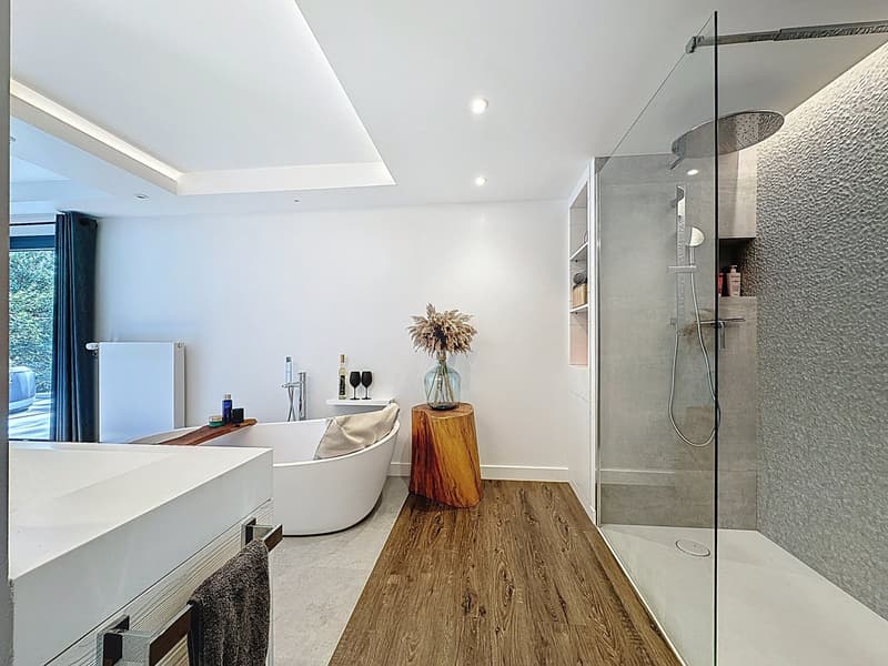 Modern bathroom with white bathtub, shower stall, wooden floor, white walls, towel rack, and view of the outdoors.