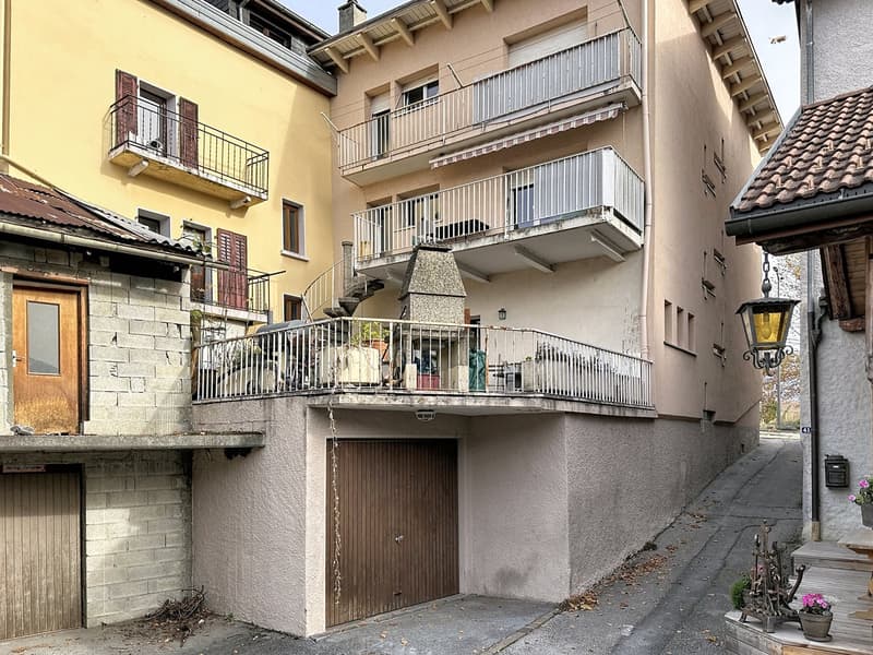 A narrow building with multiple balconies, a spiral staircase, a garage door, and a lamp.