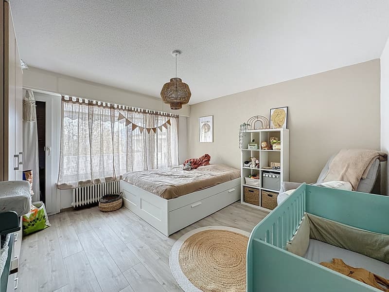 bedroom with bed, storage drawers, white and beige walls, chandelier, rug, shelves, baskets, picture frame, curtains, radiator, wicker basket, toys