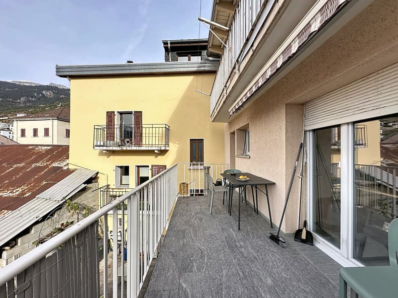 Building exterior with a balcony featuring a dining table and chairs, a tiled floor, and a view of the mountains.