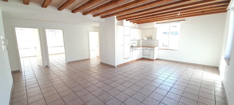 Empty room with wooden ceiling, tiled floor, white walls, open doors leading to other rooms, kitchen with dishwasher