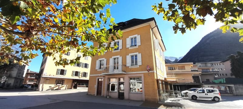 2 story building, beige color, windows with white shutters, balconies on the second floor, mountain in the background