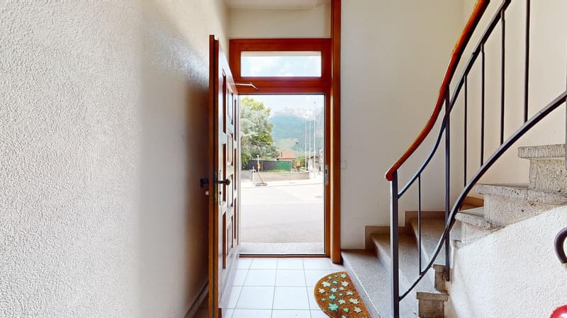 Concrete floor, white wall, open door, wooden door, stairs with handrail, view of street with mountains