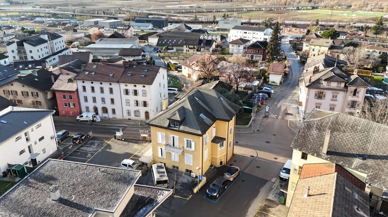 Aerial view of a neighborhood with various buildings, cars parked on the side of the road, and a car park in front of a yellow building.