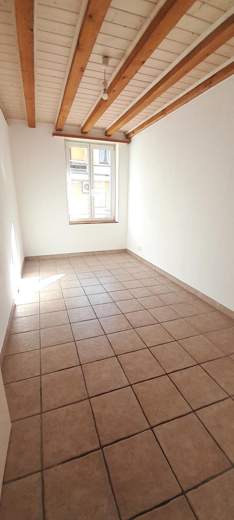 Empty room with tiled floor, wooden ceiling, white walls, single window, and ceiling lamp