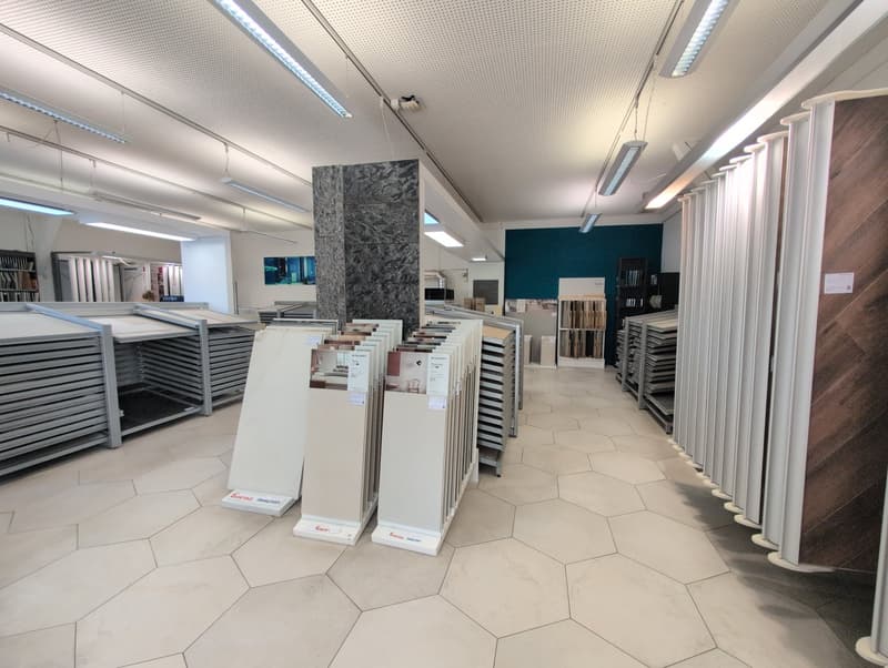 Commercial real estate: indoor showroom with hexagonal tiled flooring, displays of tiles, ceiling lighting, and a wall with a teal accent.
