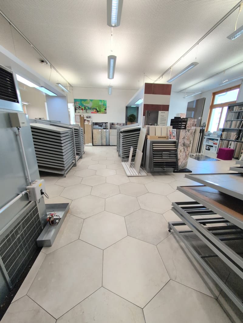 industrial store with white hexagonal tile flooring, modern lighting, various shelves with different products, a green poster on the wall, air conditioners on the side.