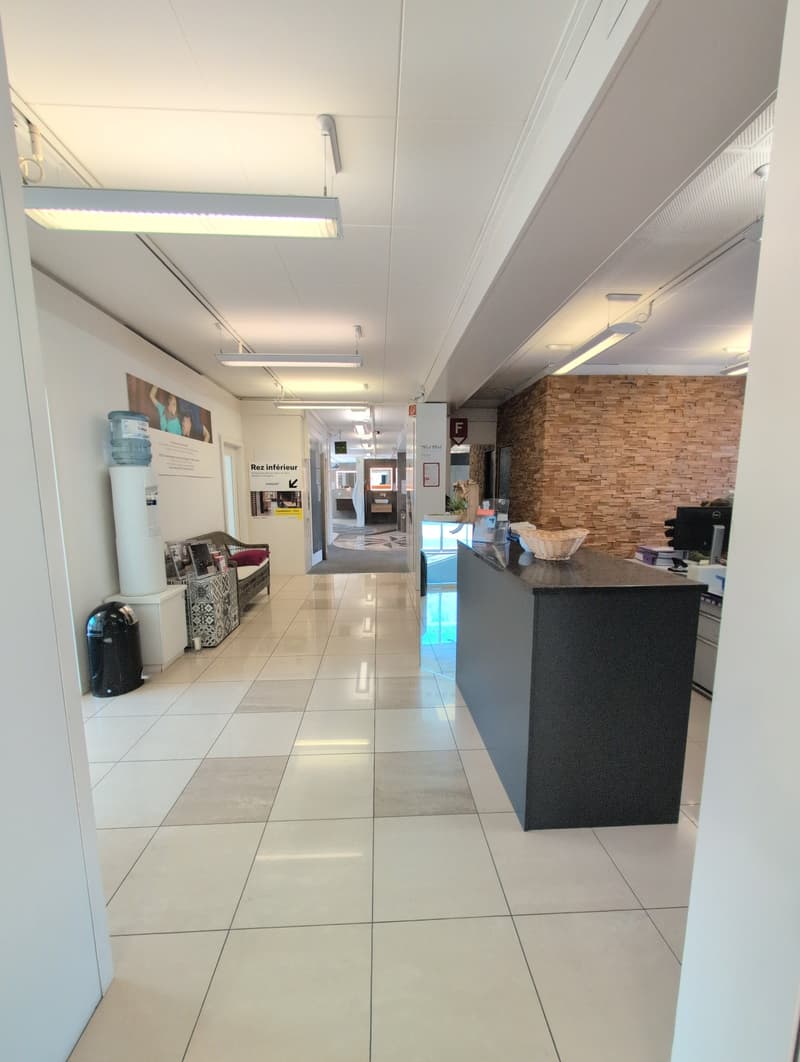 tiled floor, white walls, ceiling lights, a bench and sofa, a water dispenser, a black trash can, a reception desk with a black surface