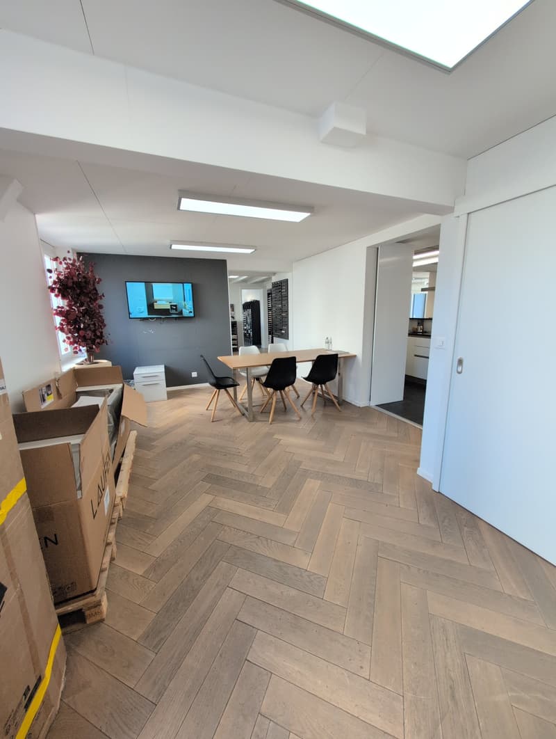 Modern office space with wooden parquet floor, dining table, chairs, and mounted TV on the wall, boxes and wooden pallet.