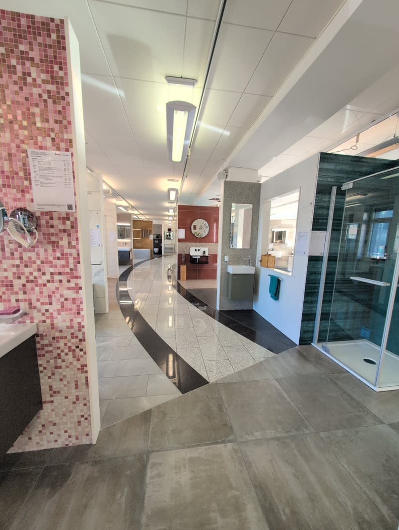 An interior view of a showroom with tiled floors, exposed ceiling with built-in lighting, and a spiral display path, featuring various washroom design elements and fixtures.
