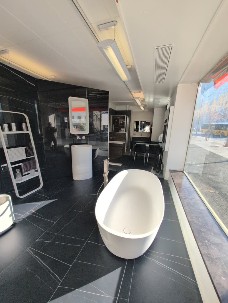 Modern bathroom with black tiled floor, modern bathtub, white countertop, modern faucet, shelves, glass windows