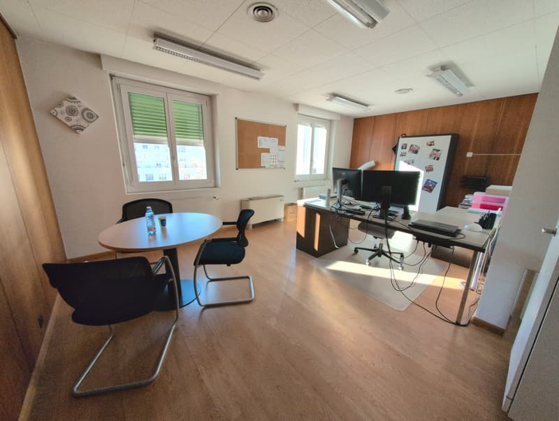 Office room with a table, chairs, a desk, computers, radiator, and a bulletin board