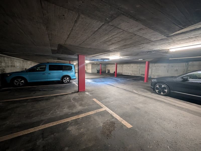 2 cars parked, illuminated by ceiling lights, parking lines, pillars