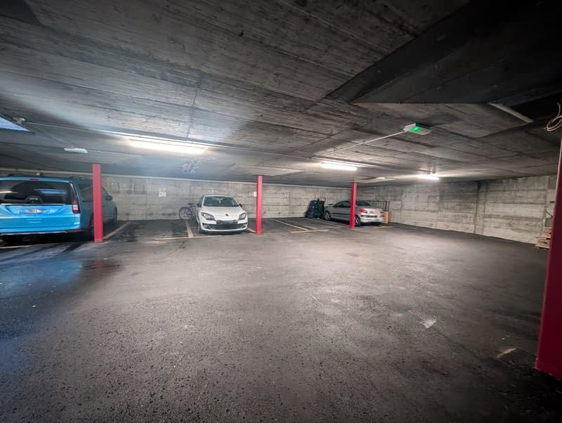 underground parking lot, three cars parked, red pillars between the parking spaces, a bicycle leaning against the wall