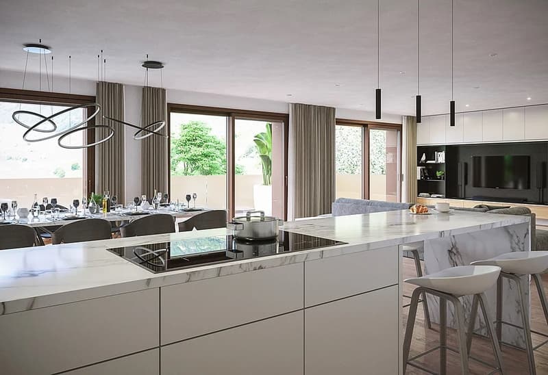 Spacious open-plan kitchen and dining area with large windows overlooking the outdoor greenery. The kitchen features a marble-topped island with a built-in cooktop and dishwasher. The dining table is set with place settings, and the room is illuminated by