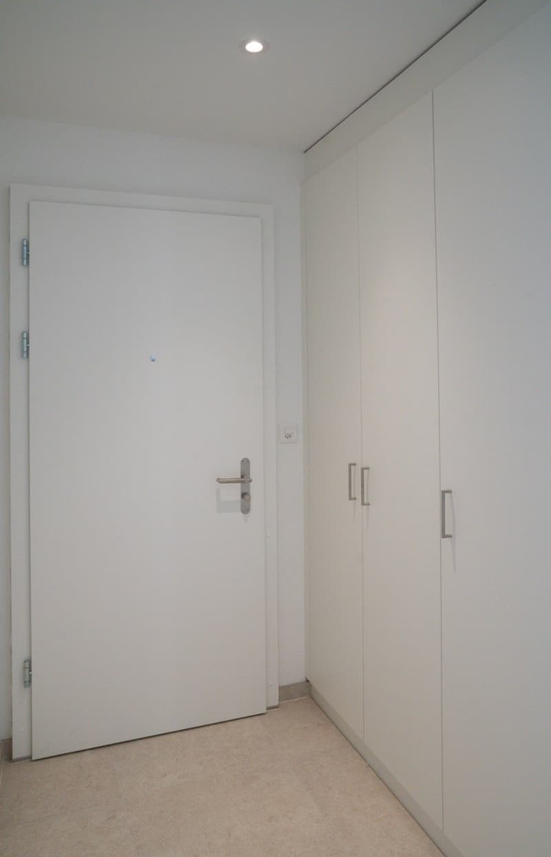 Empty room with white door, white walls, two tall white closets, tiled floor