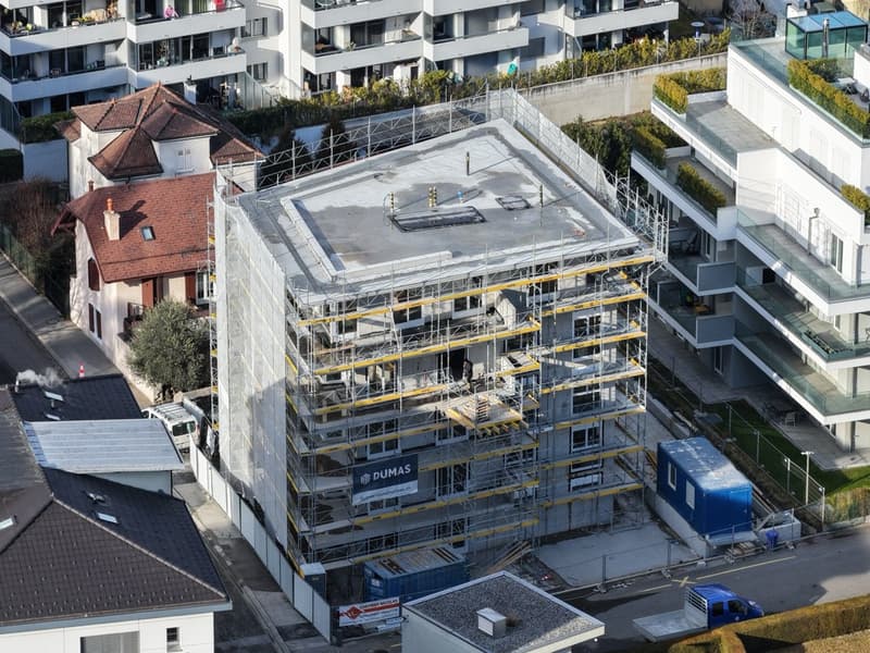 Construction site for a new building, scaffolding surrounding the structure, several neighboring buildings visible, one with a brown roof