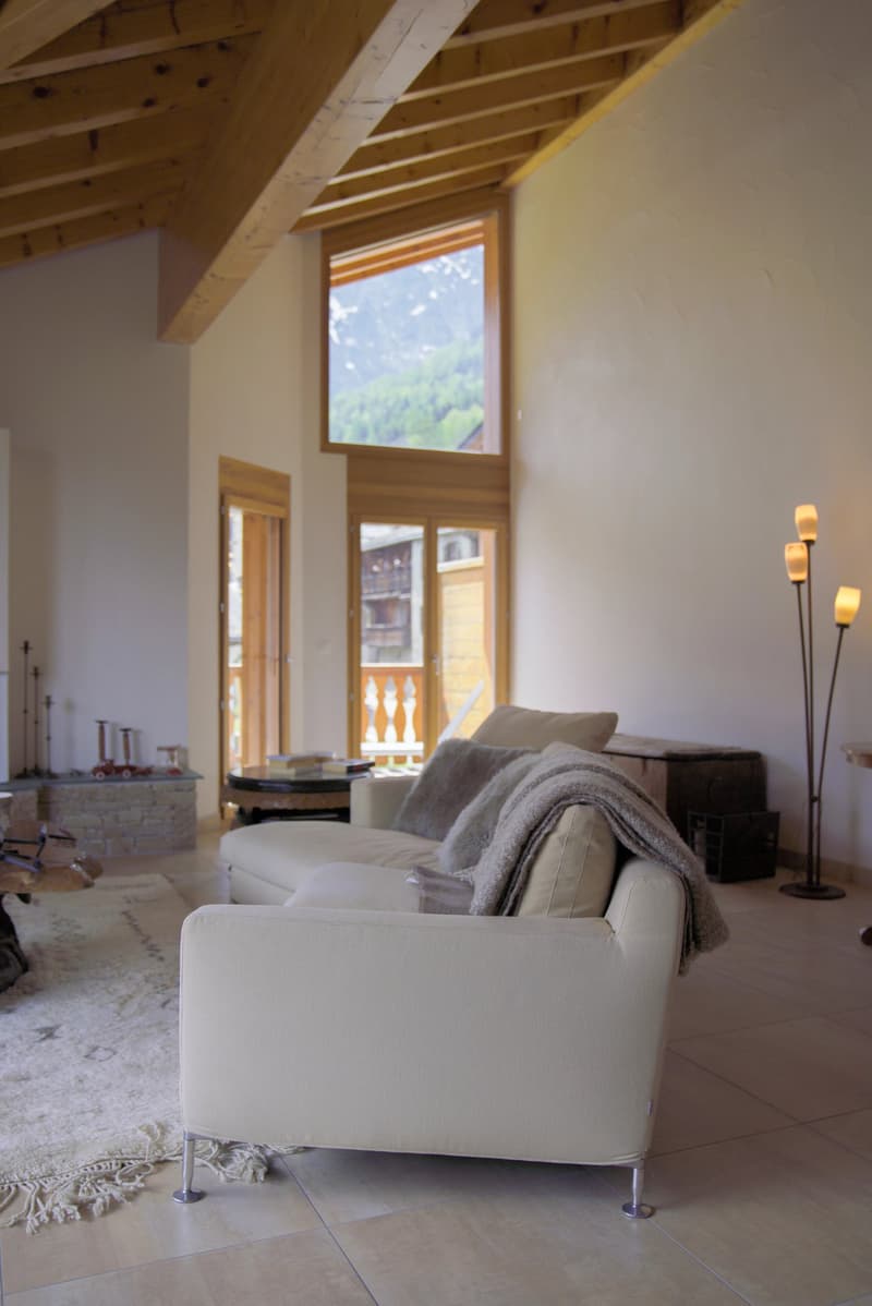 Spacious living room with high ceilings, exposed wooden beams, large windows providing a scenic view, white sofa, and floor lamps