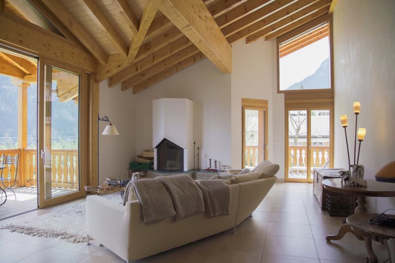 Spacious living room with high wooden ceiling, large windows, fireplace, and comfortable seating area