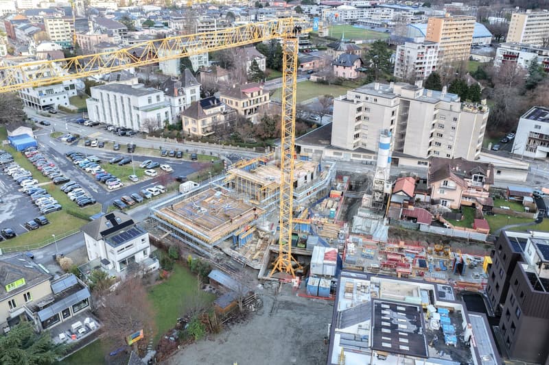 construction site with a crane, multiple buildings, a parking lot, and houses in the vicinity
