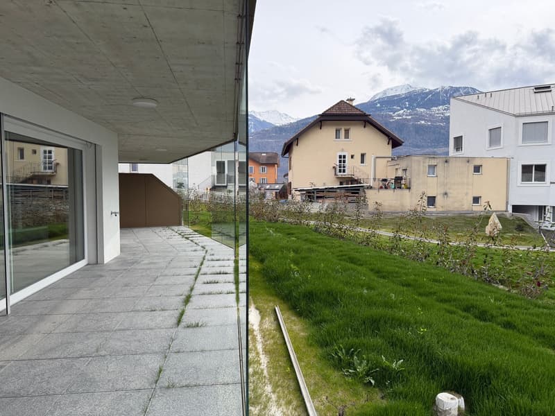 Modern building with glass walls, concrete floor, and a pathway leading to a grassy area with a view of the mountains.