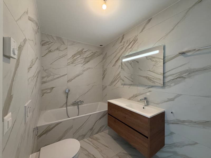 modern bathroom with white marble tiles, bathtub, sink, mirror, toilet, and shower