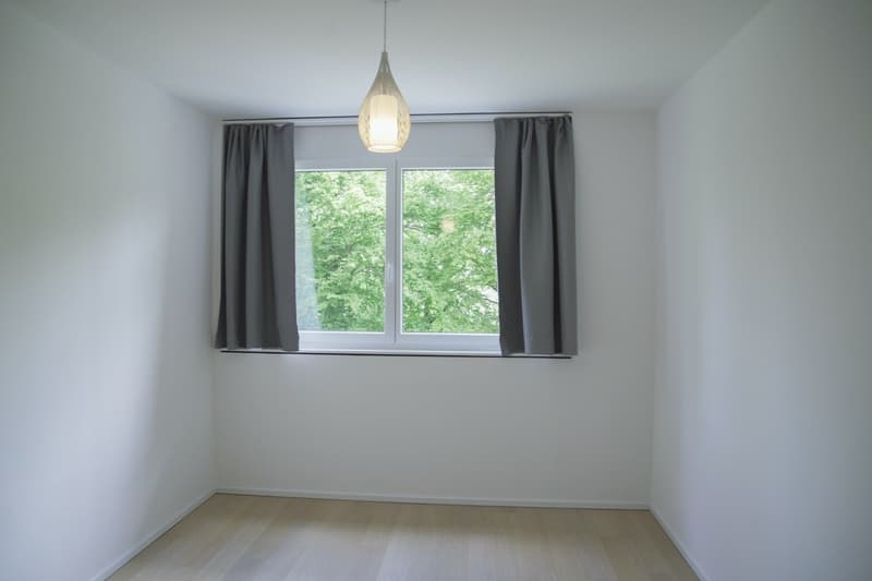 empty room, white walls, wooden floor, large window with gray curtains, pendant light