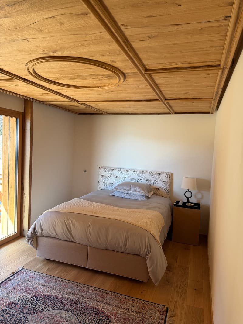 wooden ceiling, bed with floral headboard, nightstand with lamp, rug, glass door