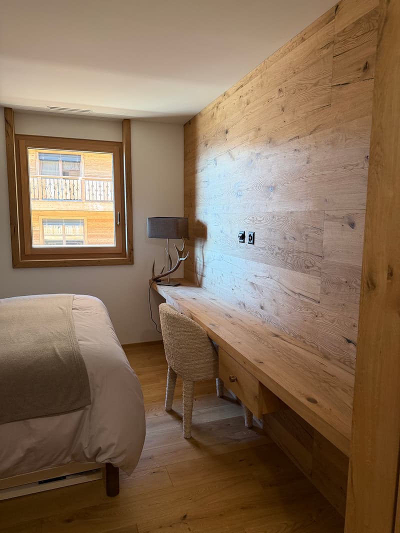 bedroom with bed, desk, chair, window, wooden wall, lamp, deer antlers