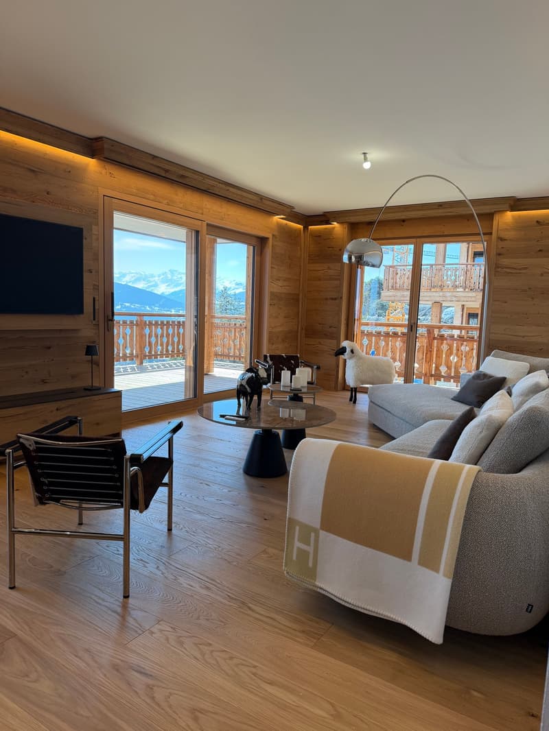 Living room with wooden walls, large windows, balcony, sofa, coffee table, TV, lamps, decorative items