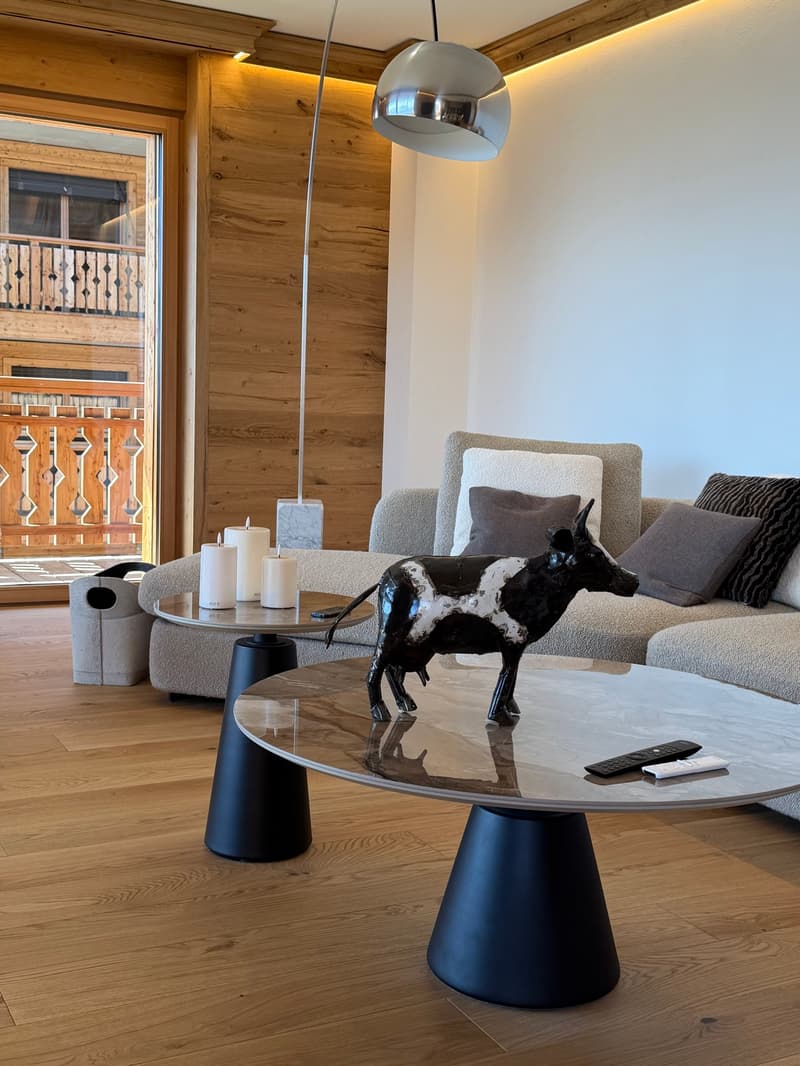 wooden floor, large couch, two tables, cow statue, remote controls, candles, lamp