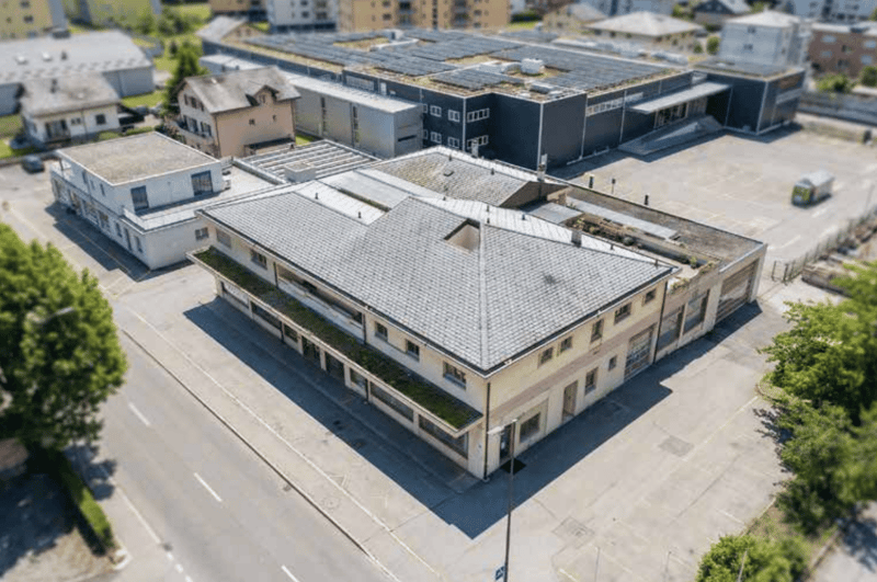 Aerial view of a building with a flat roof, multiple windows, and a parking lot in front.