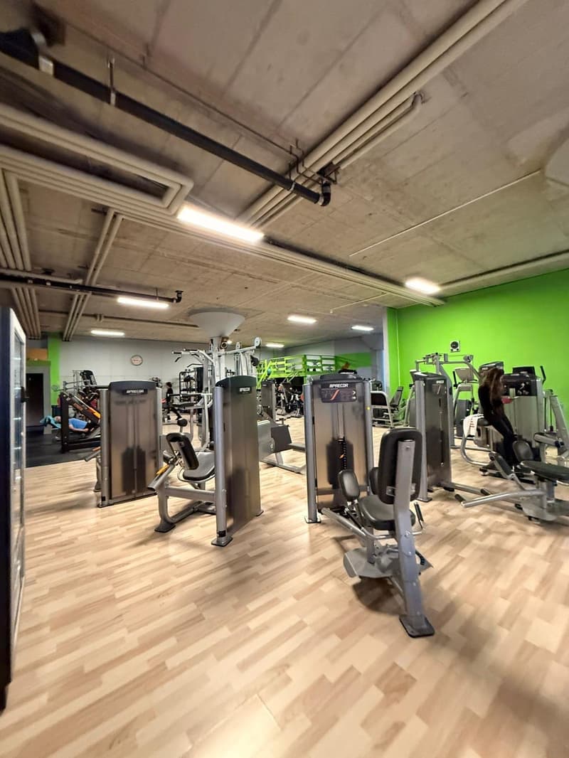 A gym with various exercise machines, wooden flooring, and green walls.