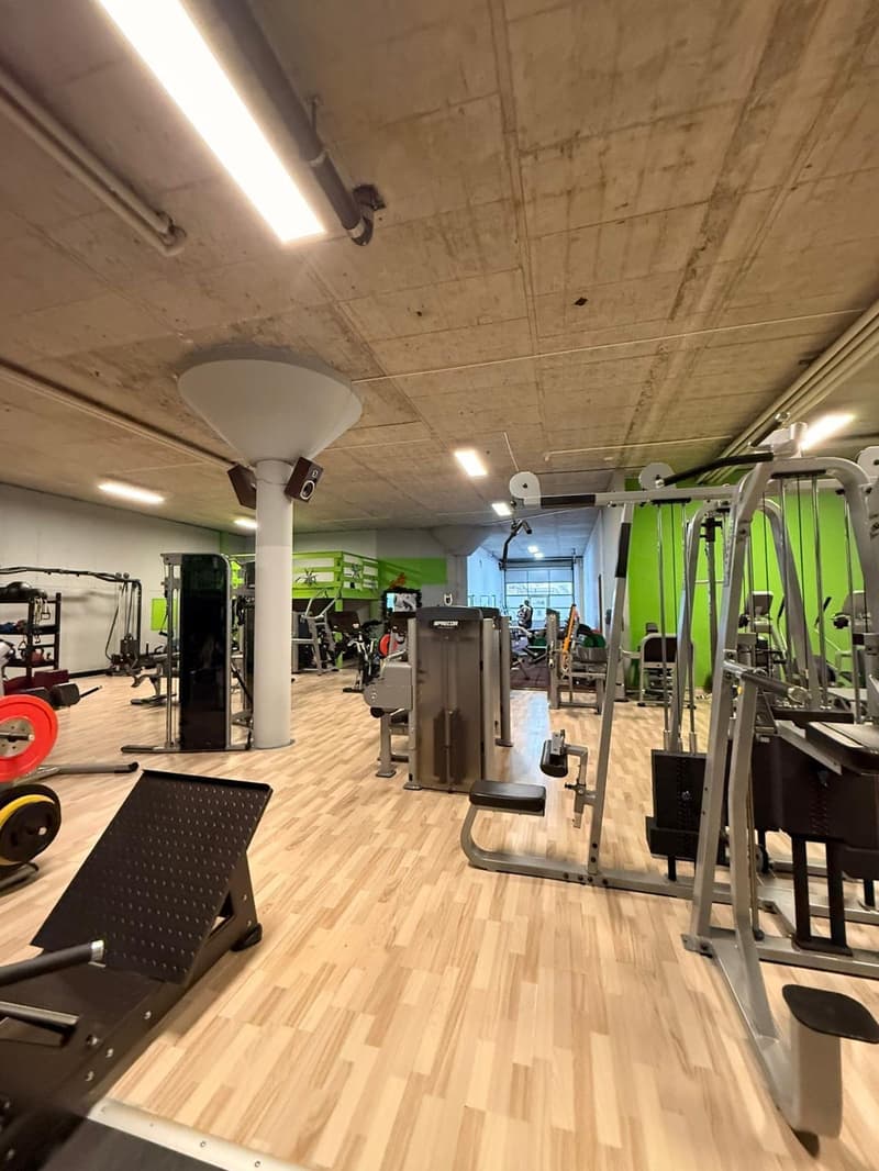 well-equipped gym with various exercise machines, wooden floor, ceiling with lights and speakers, green wall