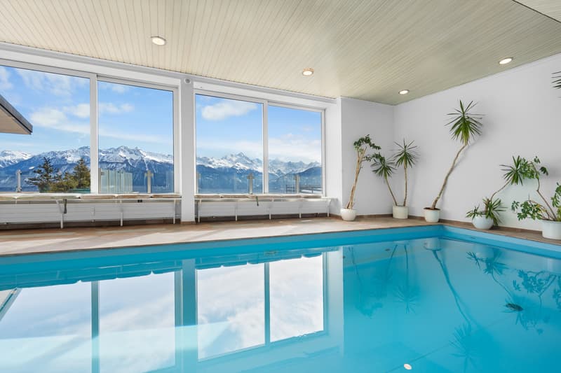 une piscine intérieure avec de grandes baies vitrées donnant sur les montagnes / an indoor swimming pool with large windows overlooking the mountains