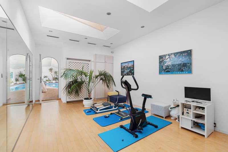 une grande pièce avec des sols bleus et des lucarnes donnant sur une piscine / a large room with blue floors and skylights overlooking a pool