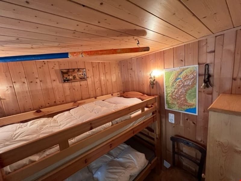 The image shows a cozy bedroom with wooden walls and ceiling. There is a bunk bed with bedding visible, and a map or poster on the wall.