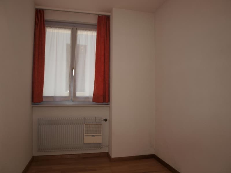 empty room, white walls, wooden floor, window with white and red curtains, radiator