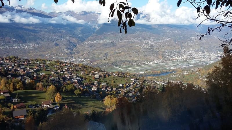 Small town in mountain valley, surrounded by green fields and trees, mountains in the background