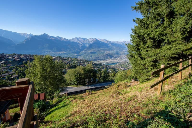 Overlooking mountains, with a distant town view, road below, wooden fences