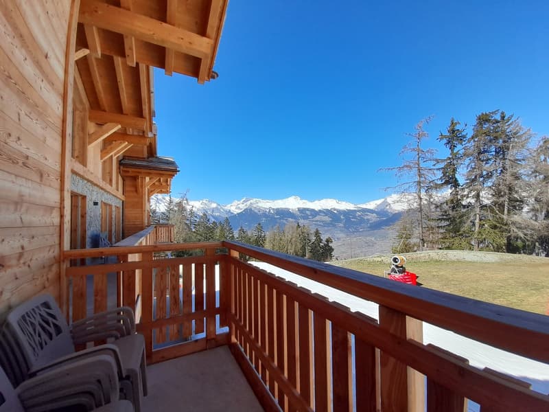 balcony with wooden railing, chairs, snow, mountains in background