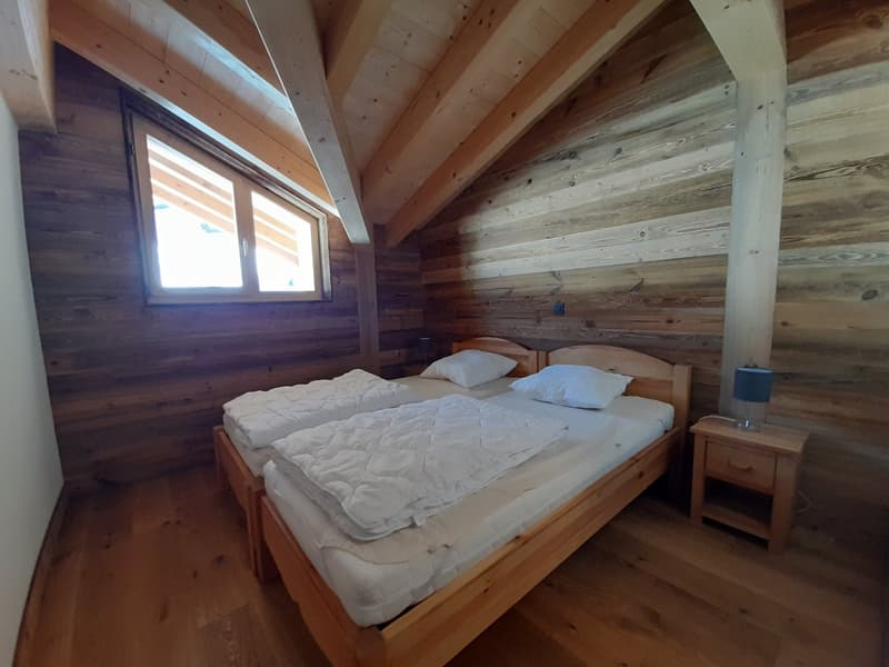 wooden walls, wooden floor, two beds, nightstand, lamp, small window