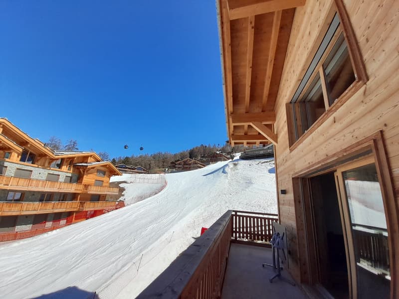 Mountain chalet, wooden construction, multiple balconies, snowy slope view, multiple buildings in background