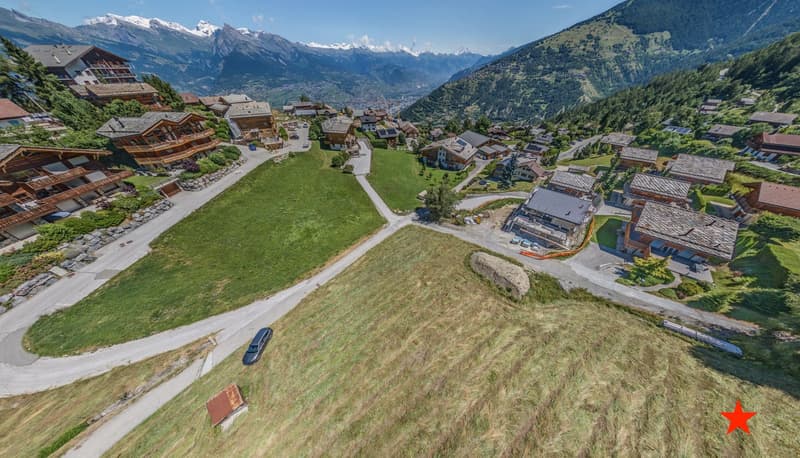 Cluster of chalets with wooden and shingle roofs, open field in front, mountain view, driveways, grass and shrubs
