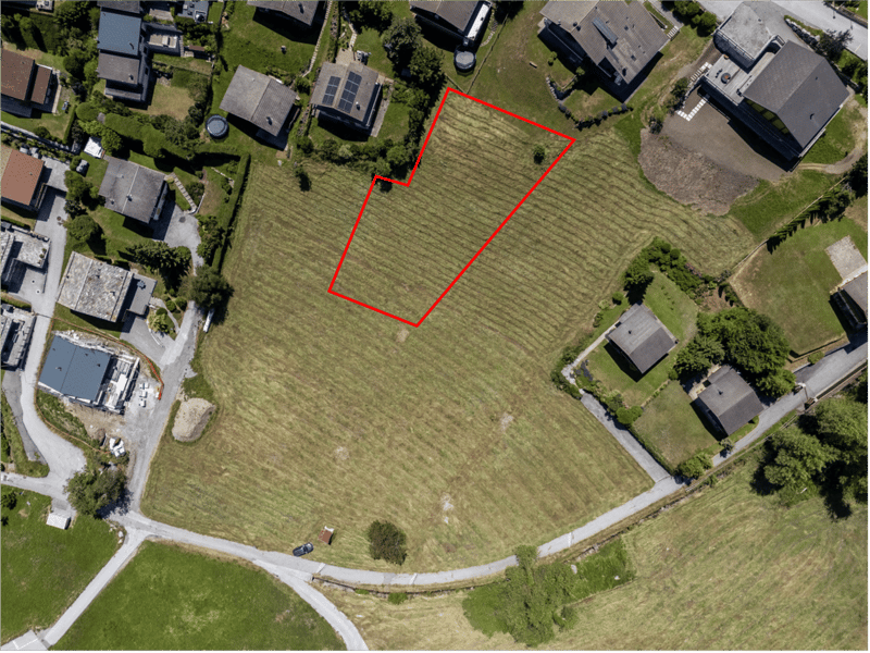 A plot of land designated for construction with an aerial view of the surroundings, featuring other houses and greenery.