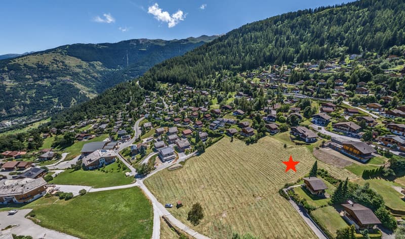 Plot in a village with mountain view, surrounded by houses and fields.