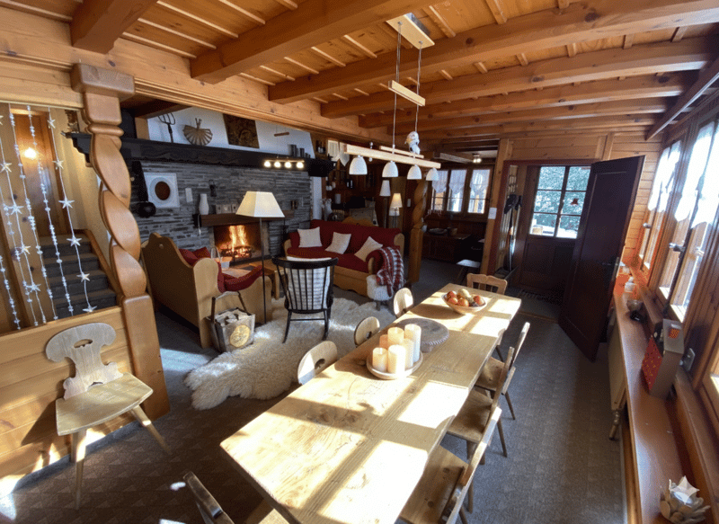 Dining room with wooden table, chairs, fireplace, wooden beams, carpet, lamps, and a rug.