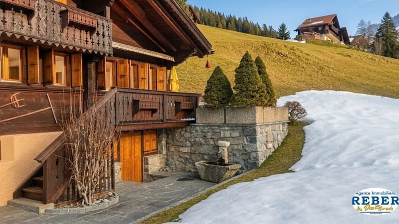 Traditional wooden chalet, wooden balcony, stone wall, snow-covered hill, trees