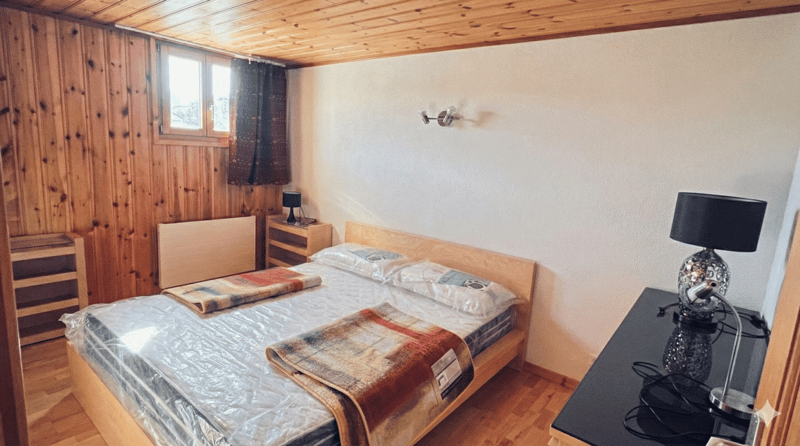 bedroom with wooden walls, bed, nightstands, lamp, radiator, window with curtains