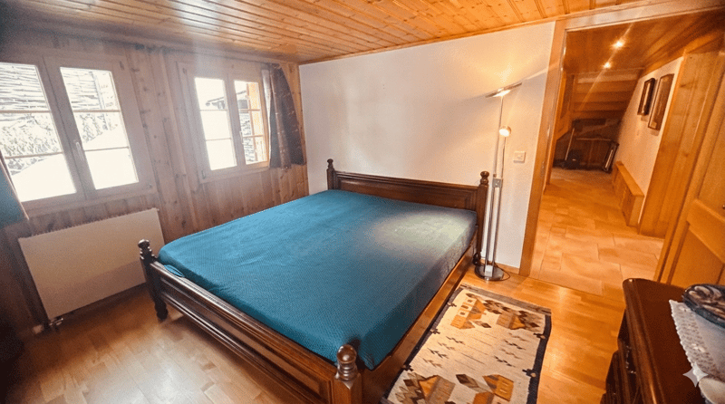 bedroom with wooden bed, blue bedspread, wooden floor, wooden walls, windows, radiator, floor lamp, rug